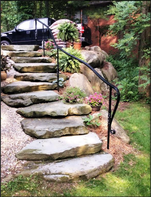 Metal Handrail installed on stone steps leading to a garden, providing safety and style in outdoor settings.