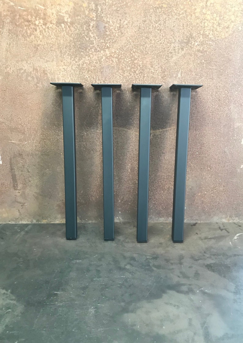 Metal Table Legs 1.5x1.5 single post flat black set of 4 standing on a textured surface.